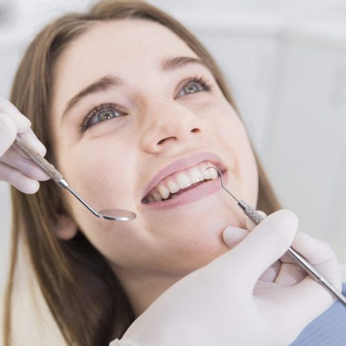 smiling-young-woman-having-teeth-examined-dentists