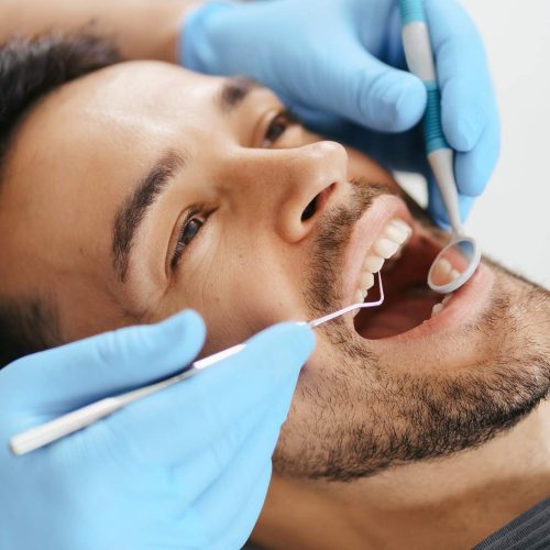 sonriente-joven-sentado-silla-dentista-mientras-medico-examina-sus-dientes